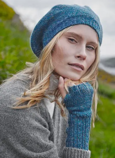 Blonde woman wearing blue beret and matching handwarmers against grassy background